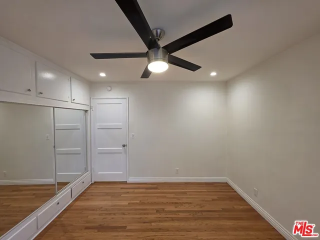 a view of an empty room with wooden floor and a ceiling fan