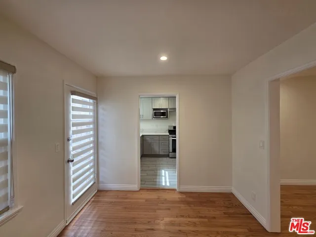 a view of empty room with wooden floor and kitchen