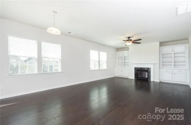 an empty room with wooden floor fireplace and windows