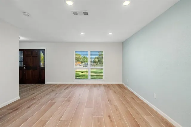 a view of an empty room with wooden floor and a window