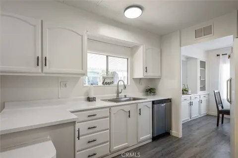 a kitchen with a sink dishwasher a stove and white cabinets with wooden floor