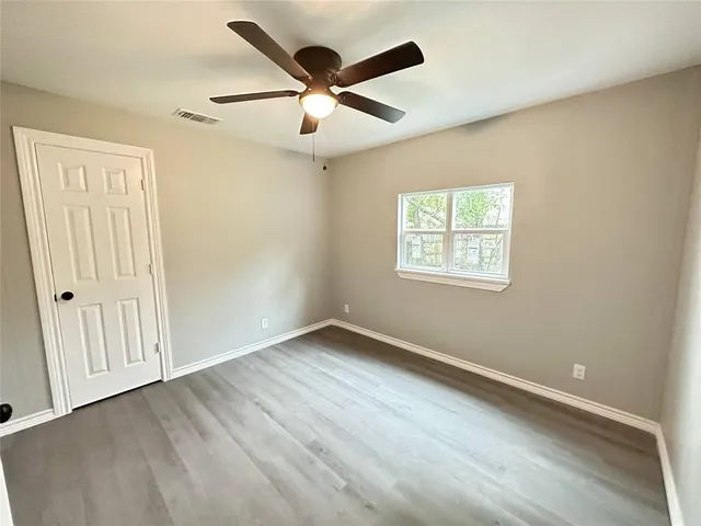 an empty room with wooden floor ceiling fan and windows