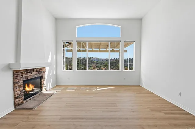 a view of an empty room with wooden floor fireplace and a window