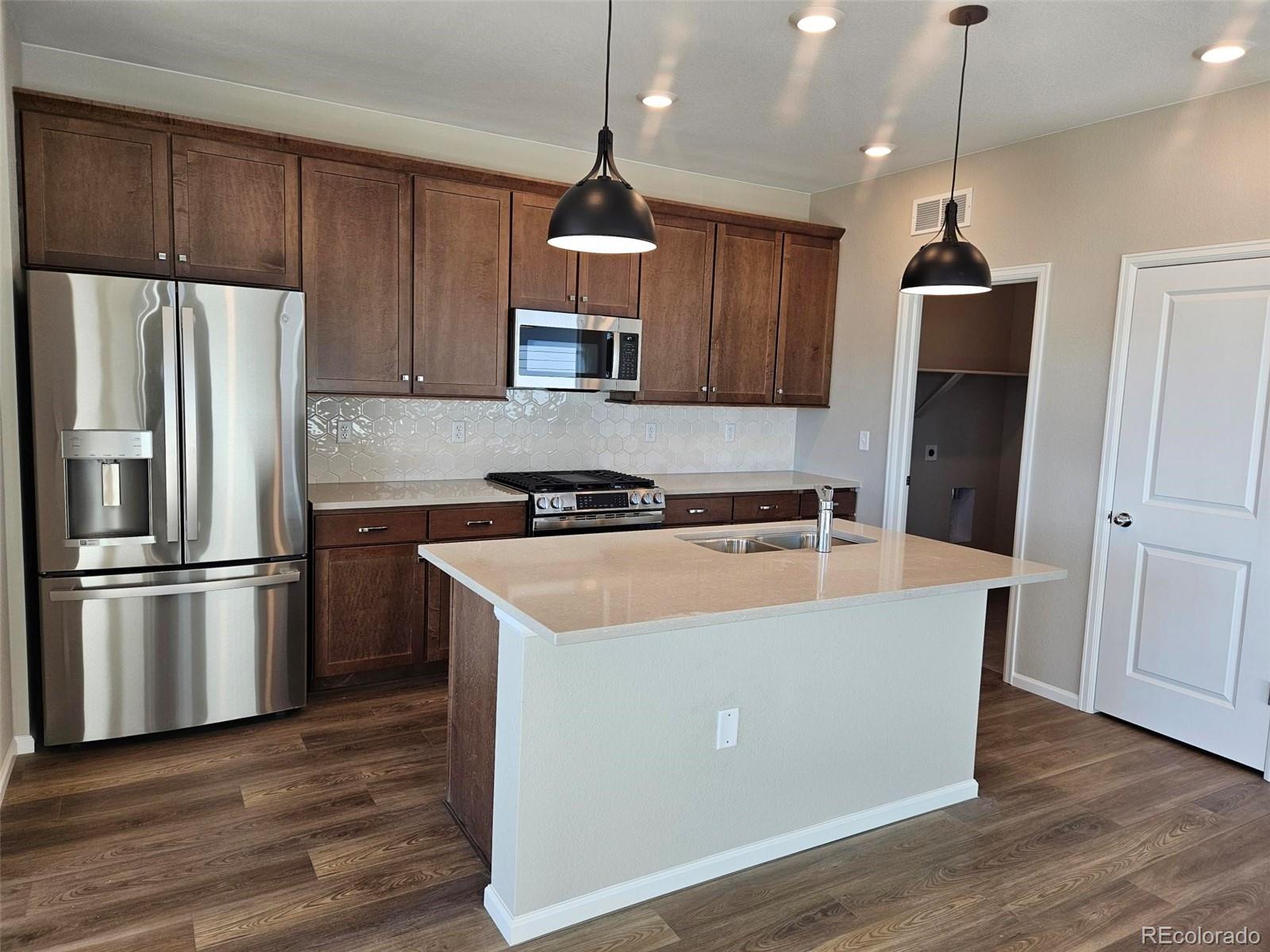 6028 Keyser Place Brighton, CO 80601 - Photo 7 of 14 a kitchen with kitchen island a refrigerator a stove a wooden floor and a window