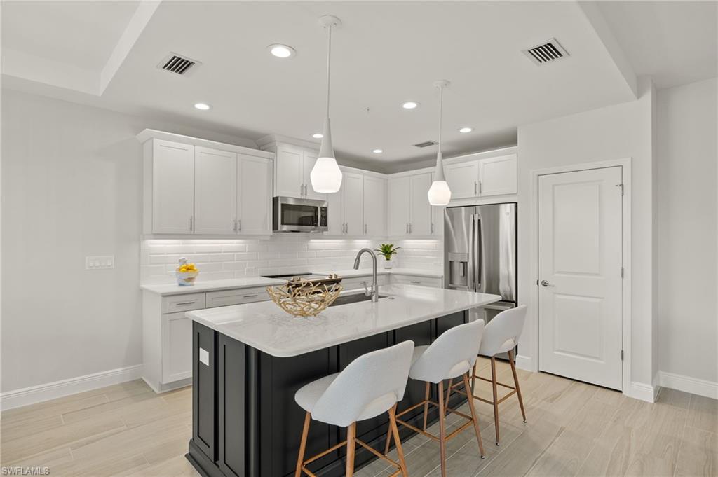 2647 Seychelles Circle, Unit 2203 Naples, FL 34112 - Photo 4 of 32 a kitchen with stainless steel appliances kitchen island granite countertop a table chairs stove and white cabinets