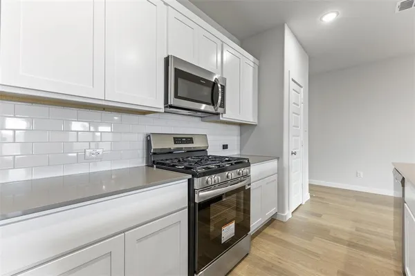 a kitchen with stainless steel appliances granite countertop grey cabinets a stove top oven a sink and dishwasher