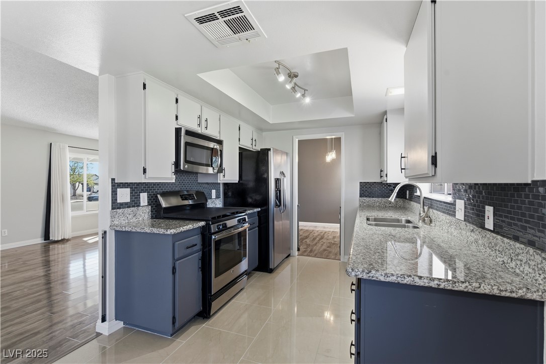 782 Darlene Way Boulder City, NV 89005 - Photo 13 of 39 Kitchen featuring light stone countertops, stainless steel appliances, white cabinetry, backsplash, and a raised ceiling