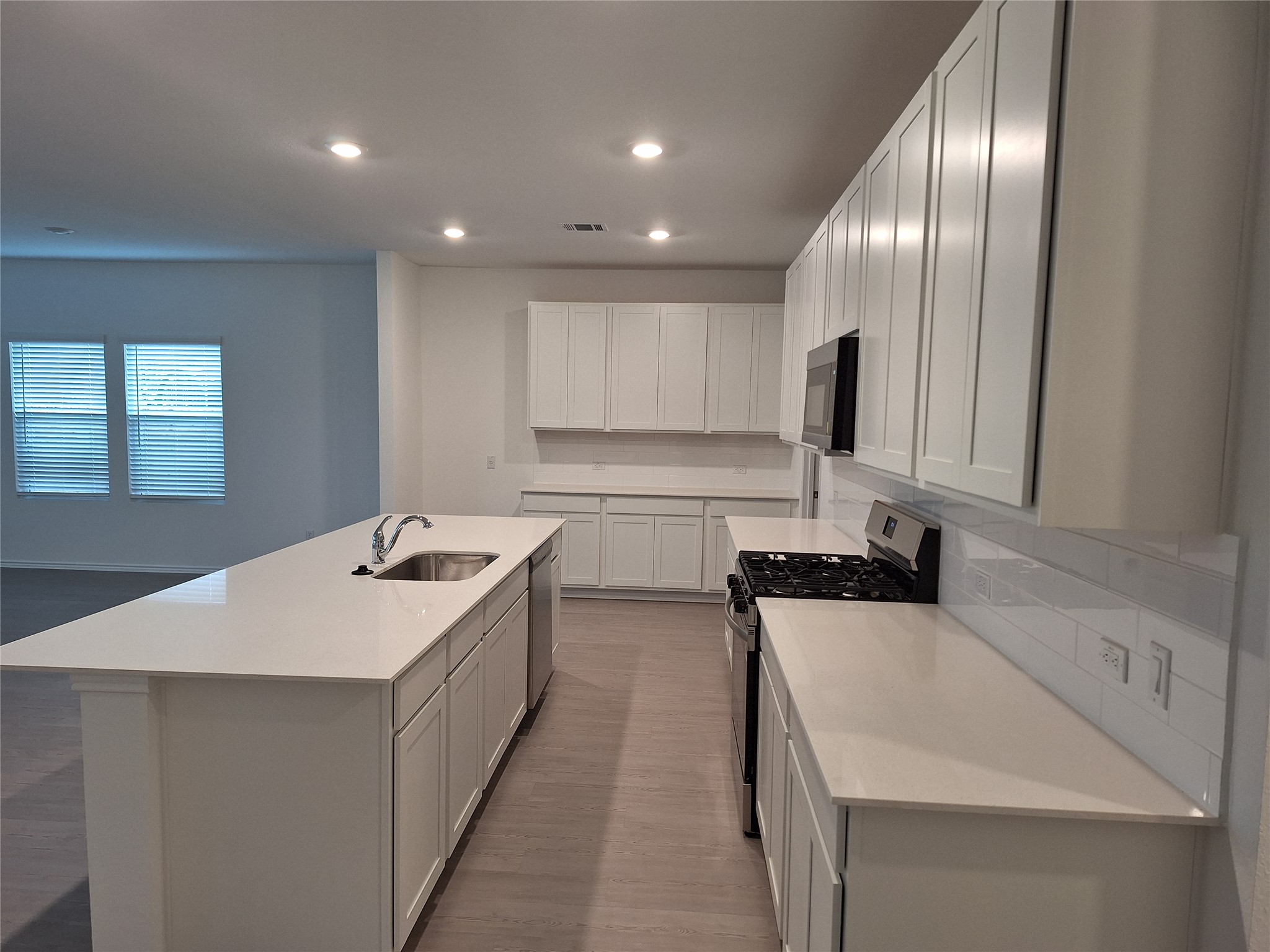 18001 Prairie Falcon Way Pflugerville, TX 78660 - Photo 24 of 38 Contemporary kitchen featuring a large island with an undermount sink, white cabinetry, integrated stainless steel appliances, white countertops, and a subway tile backsplash