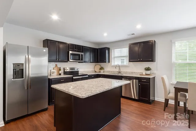 a kitchen with stainless steel appliances granite countertop a stove a sink dishwasher a refrigerator and a microwave oven with wooden floor