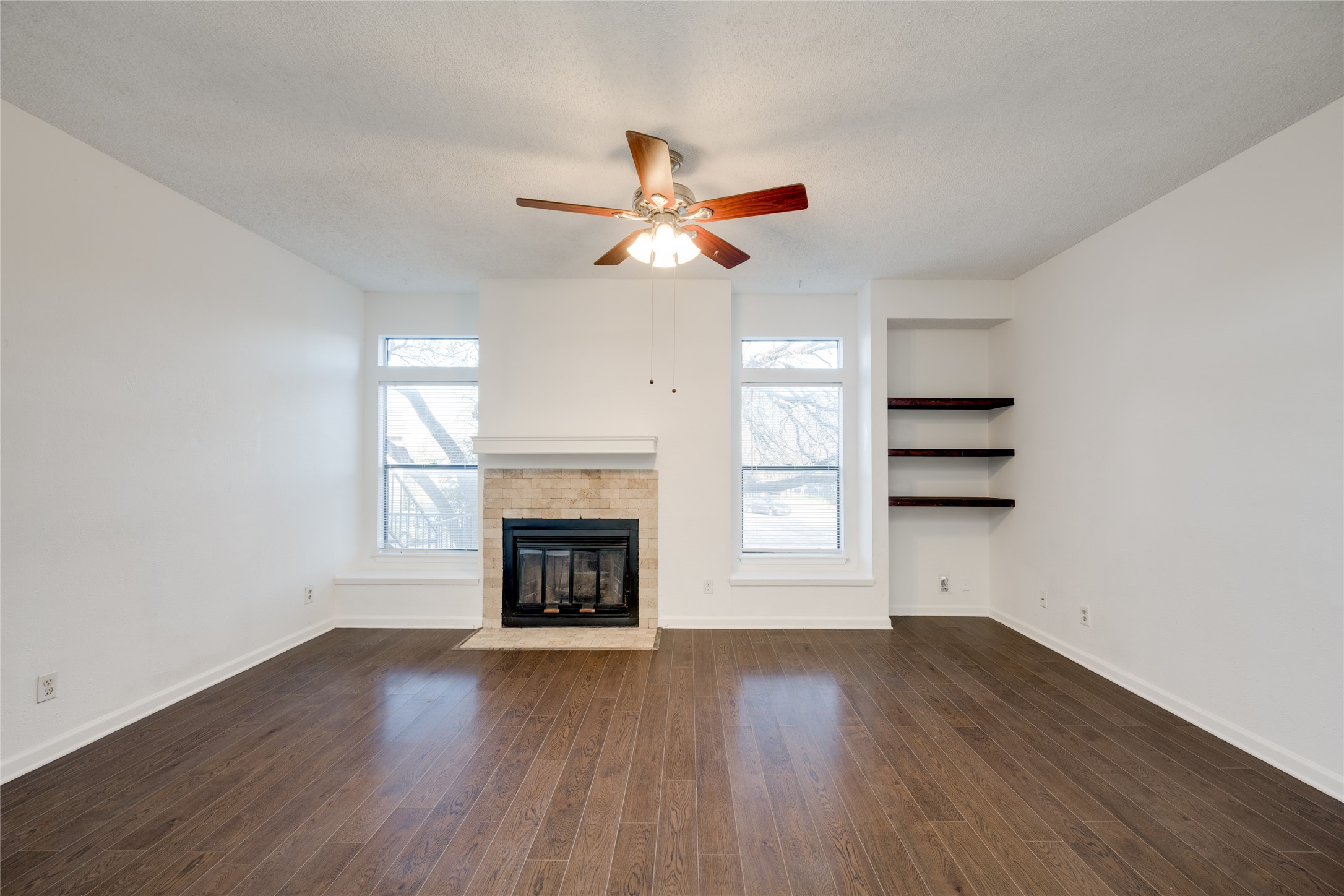 5304 Indio Cove, Unit B Austin, TX 78745 - Photo 6 of 40 an empty room with wooden floor a ceiling fan a fireplace and windows
