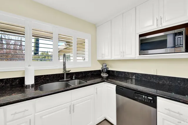 a kitchen with granite countertop white cabinets sink and window