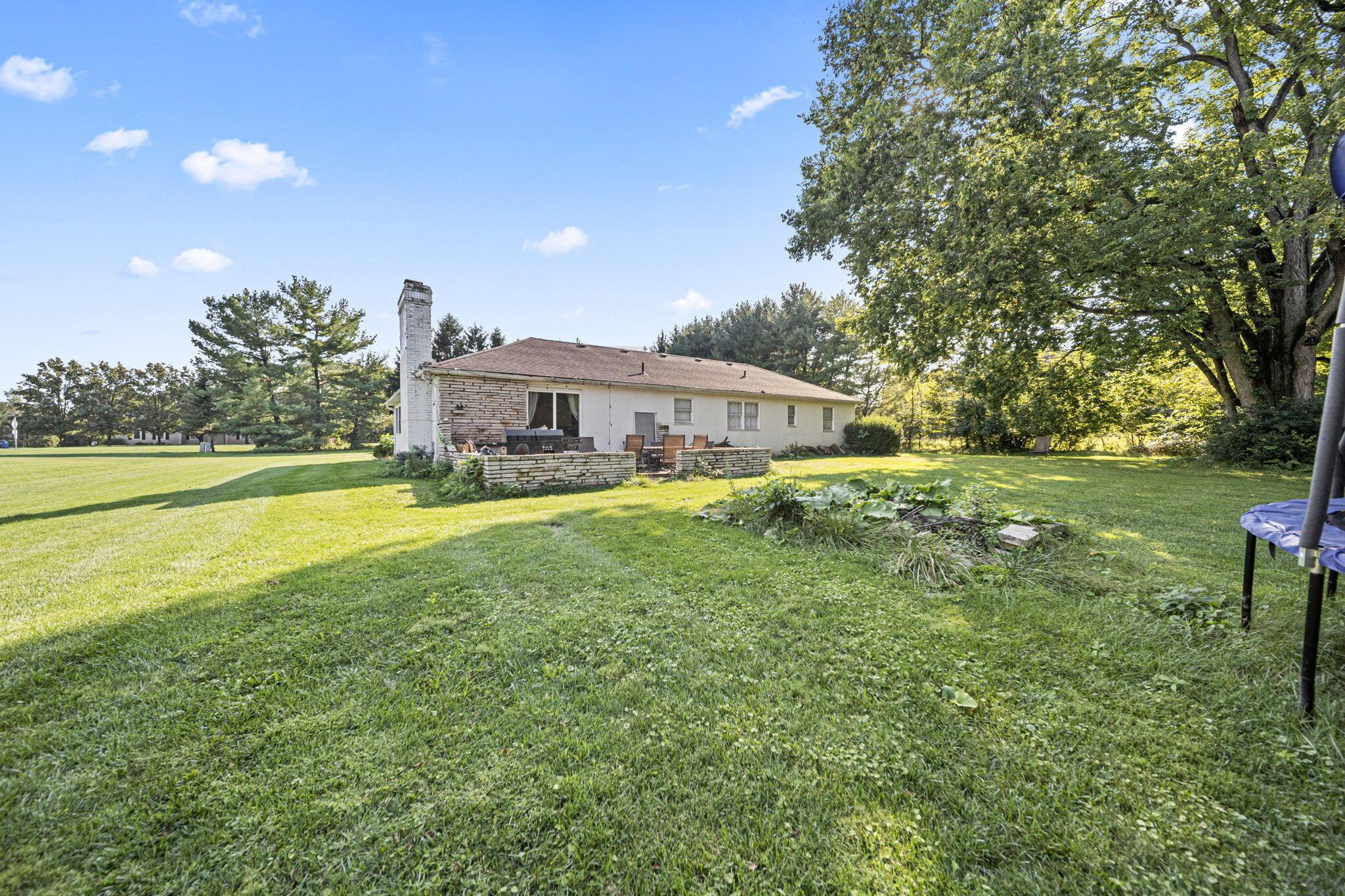 6344 Post Road Dublin, OH 43017 - Photo 31 of 45 Expansive rear yard with a stone-clad exterior, a stone chimney, and a stone patio