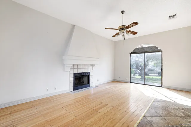 an empty room with windows chandelier fan and fireplace