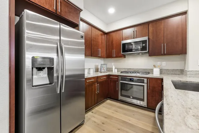 a kitchen with stainless steel appliances granite countertop a refrigerator a stove and a sink with wooden floor