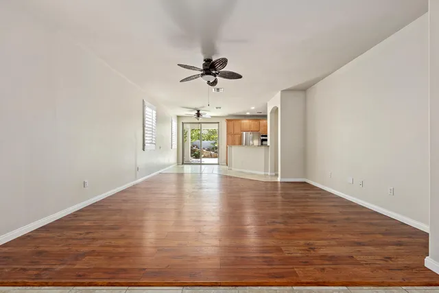 an empty room with wooden floor ceiling fan and windows