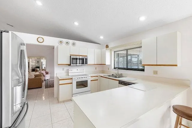 a kitchen with stainless steel appliances granite countertop a stove top oven a sink a refrigerator and white cabinets with wooden floor