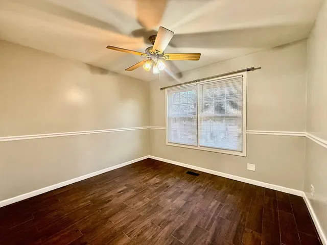 an empty room with wooden floor fan and windows