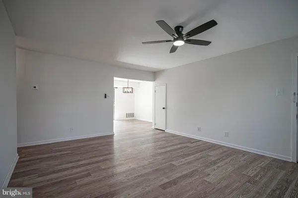 a view of an empty room with wooden floor and a ceiling fan