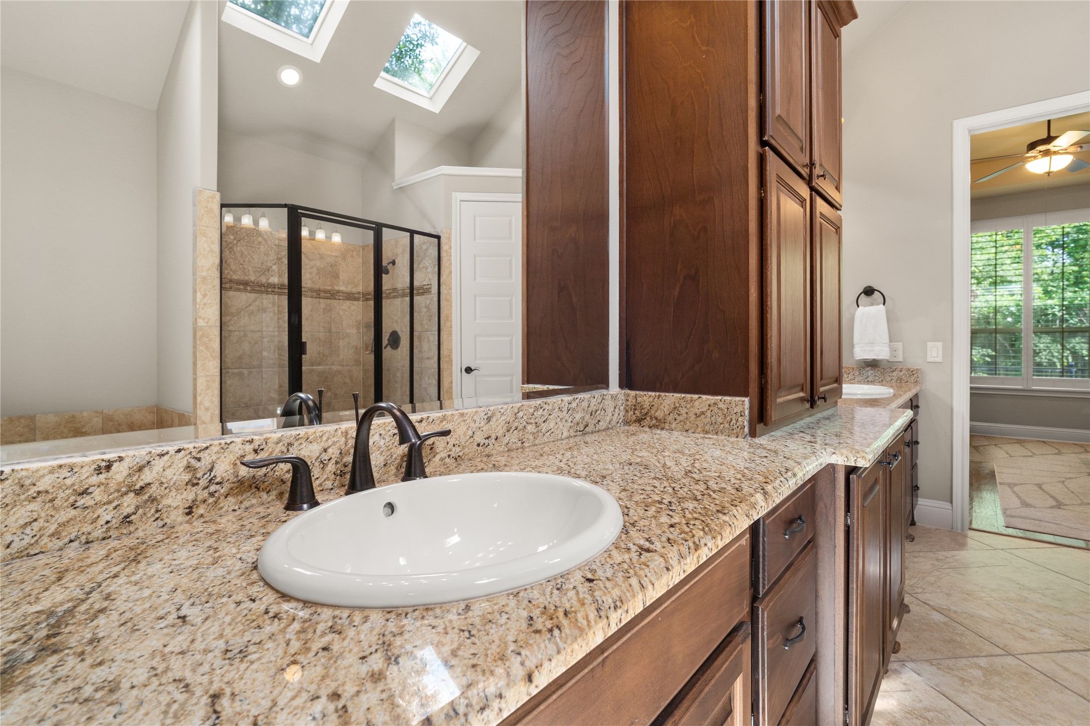19813 Cullen Ridge Drive Porter, TX 77365 - Photo 25 of 44 Get ready here in this elegant bathroom featuring stunning granite countertops, rich wooden cabinetry, and abundant natural light from skylights, creating a warm and inviting space.