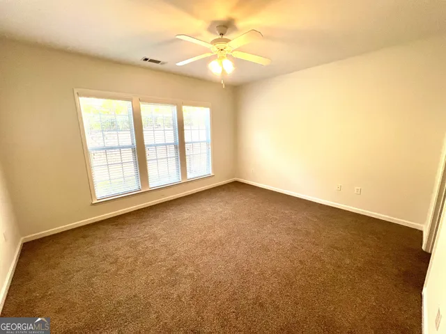 an empty room with a chandelier fan and windows