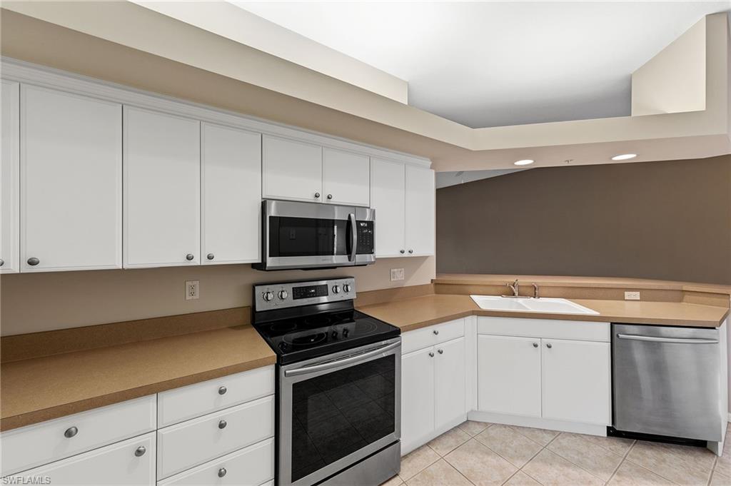 23810 Costa Del Sol Road, Unit 203 Estero, FL 34135 - Photo 9 of 48 Kitchen with appliances with stainless steel finishes, white cabinetry, light tile patterned floors, and a peninsula