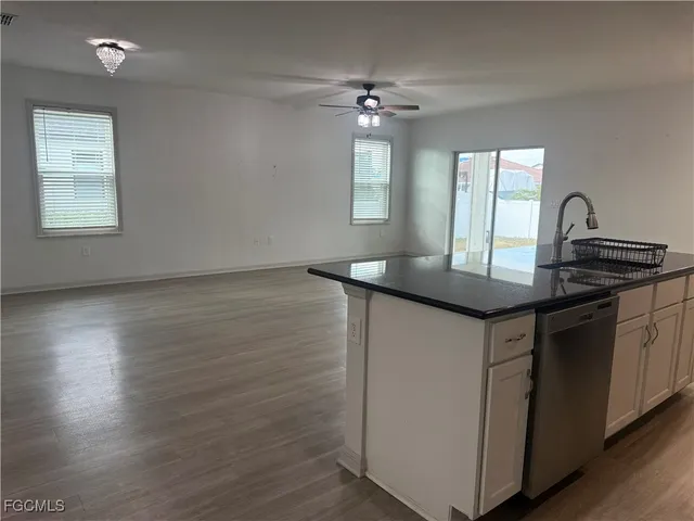 an empty room with wooden floor a ceiling fan and kitchen view