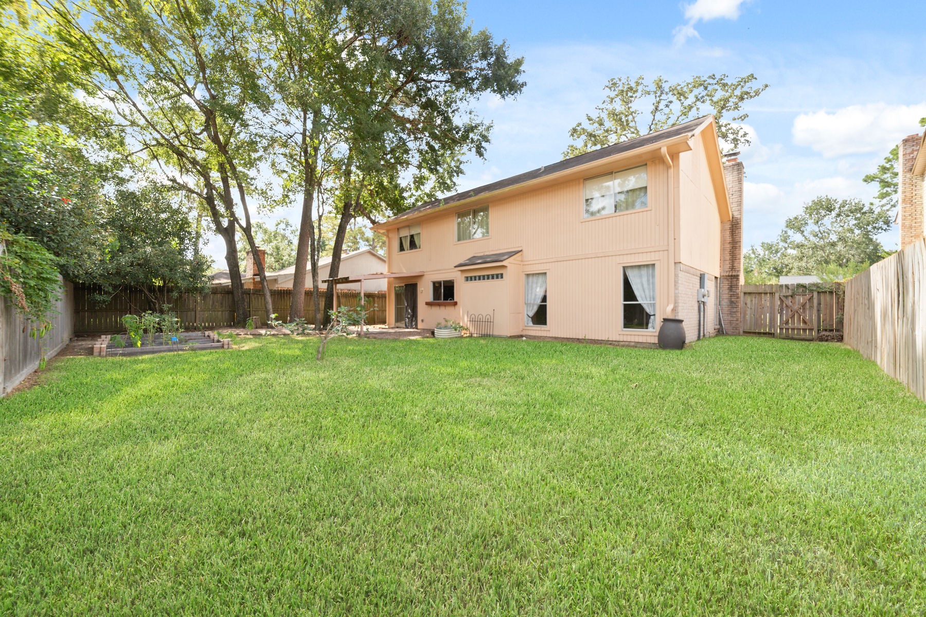 25402 Mill Pond Lane Spring, TX 77373 - Photo 8 of 24 Spacious backyard with lush green lawn, mature trees, and garden area. Two-story house with large windows, wooden fence, and a cozy patio. Perfect for outdoor activities and relaxation.