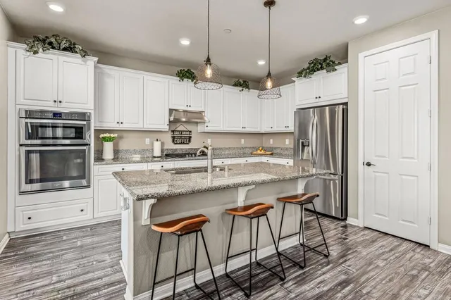 a kitchen with stainless steel appliances granite countertop a refrigerator a stove a sink a dining table and chairs with wooden floor