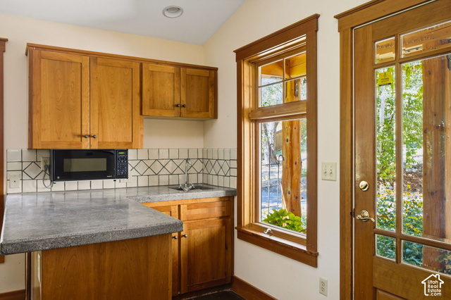 725 Canyon Road Smithfield, UT 84335 - Photo 48 of 100 Wood-finish cabinetry with dark hardware, stone-finish countertops, tiled backsplash, under-cabinet microwave, and a multi-pane window