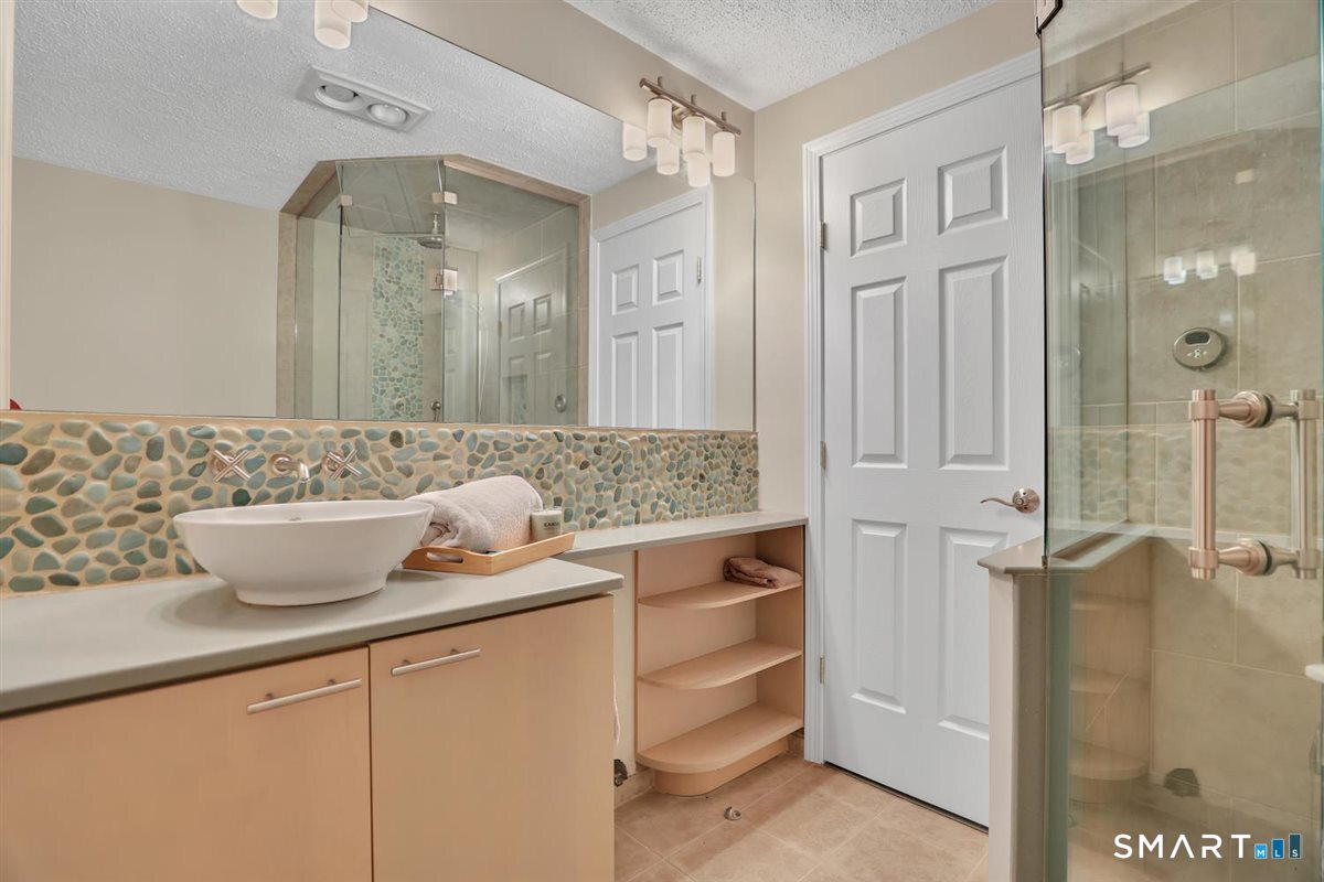 122 Ridgeview Circle Guilford, CT 06437 - Photo 27 of 40 Updated full bath on the lower/first floor offers tiled flooring, steam shower w/tile surround & glass enclosure, vanity w/built-ins and vessel sink. A door leads to outdoor patio/pool area for easy access.