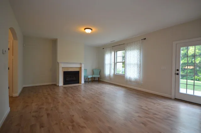an empty room with wooden floor fireplace and windows