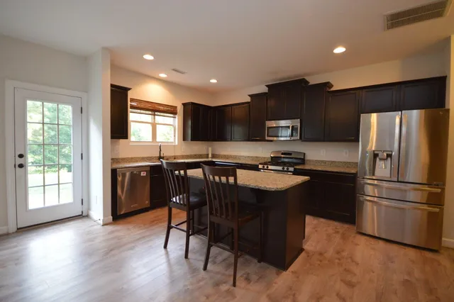 a kitchen with stainless steel appliances granite countertop a refrigerator a sink dishwasher a stove and a microwave oven with wooden floor