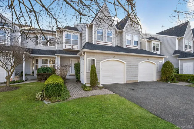 a view of a white house with a large windows and a yard with plants and a large tree