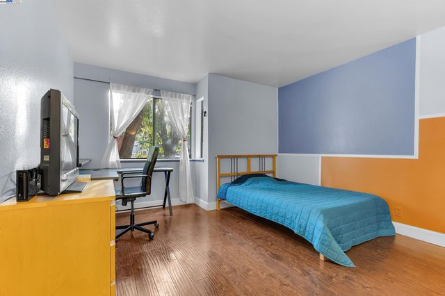 a bedroom with a bed a table and dresser with wooden floor