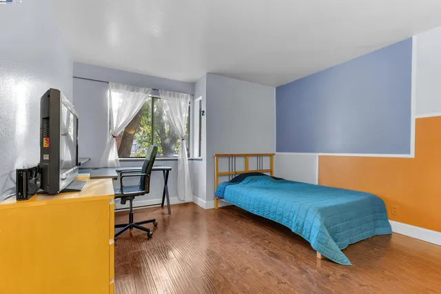 a bedroom with a bed a table and dresser with wooden floor