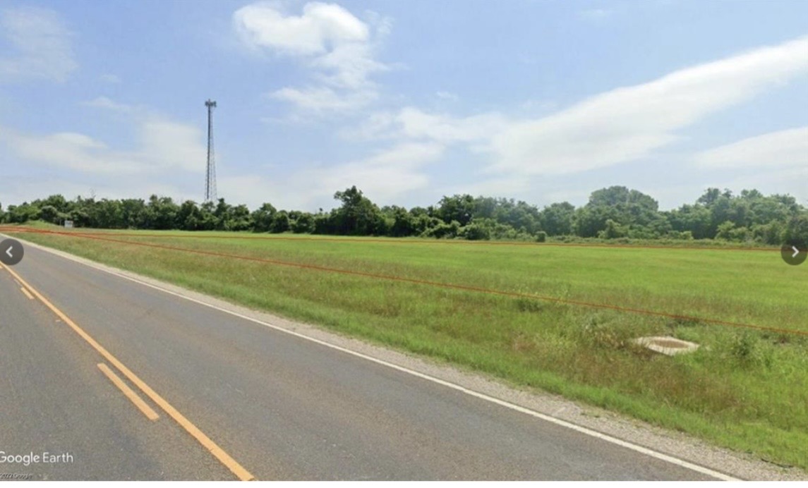 The property features an expansive green field with a tree line in the background and road frontage