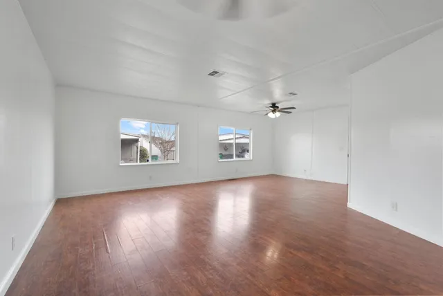 an empty room with wooden floor chandelier fan and windows