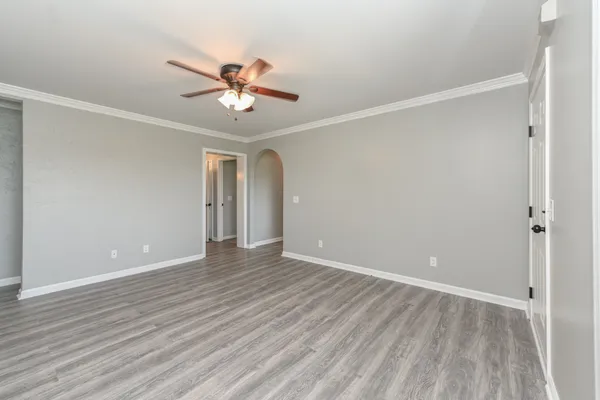 a view of an empty room with wooden floor and a ceiling fan