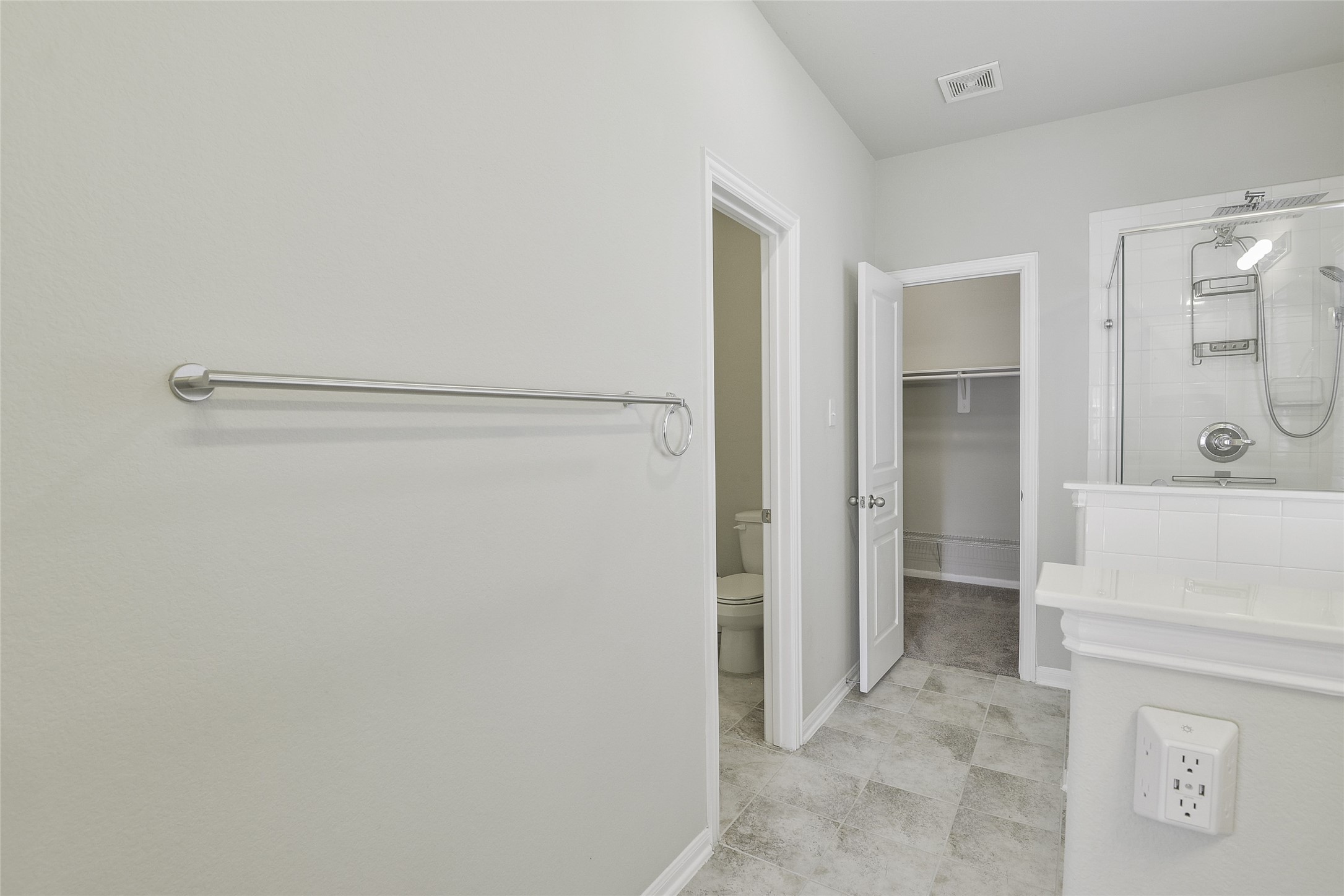 614 Pequin Road Crosby, TX 77532 - Photo 20 of 43 This photo shows a modern bathroom with light gray tile flooring, a glass-enclosed shower, and a door leading to a walk-in closet. The walls are painted in a soft neutral tone, and there's a towel bar on one side.