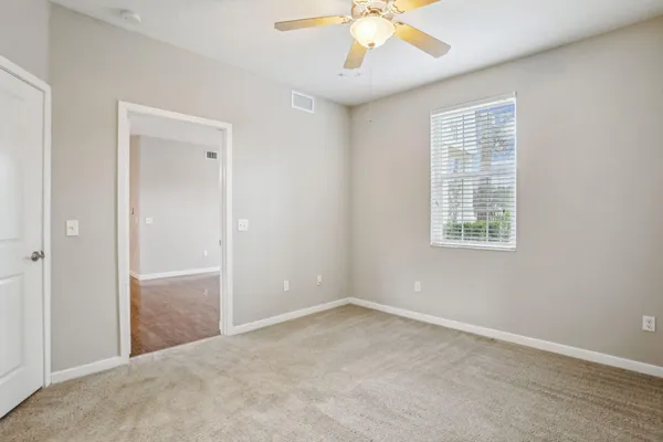 an empty room with chandelier fan and windows