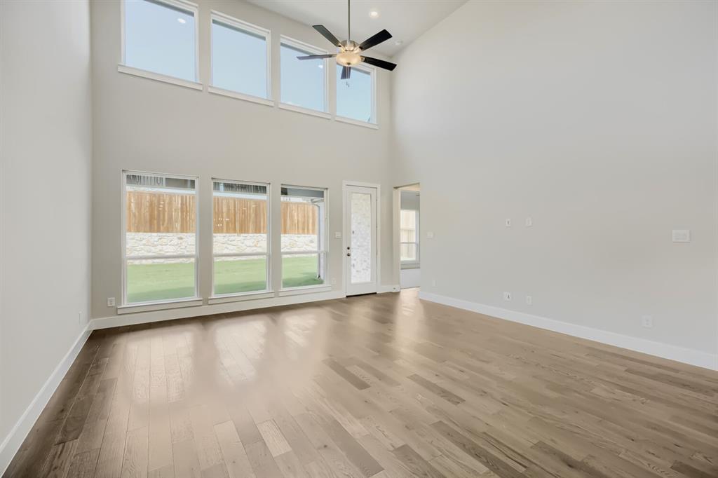 4407 Windy Point Road Oak Point, TX 75068 - Photo 3 of 27 Expansive living space featuring soaring ceilings, wood-finish flooring, a contemporary ceiling fan, and multiple windows providing views of the outdoor area with a wood fence and stone accent wall