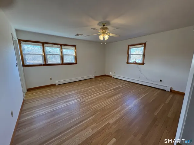 a view of an empty room with wooden floor and a ceiling fan