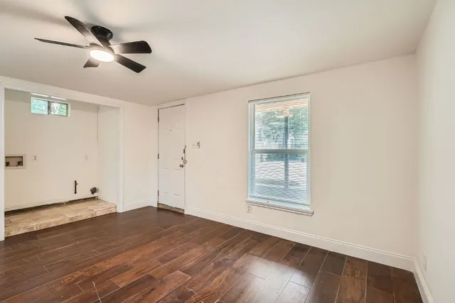an empty room with wooden floor ceiling fan and windows
