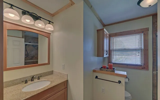 a bathroom with a granite countertop sink vanity mirror and toilet