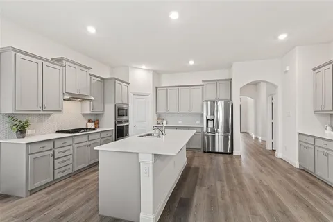 a large kitchen with stainless steel appliances a large counter top a stove a refrigerator cabinets and wooden floor