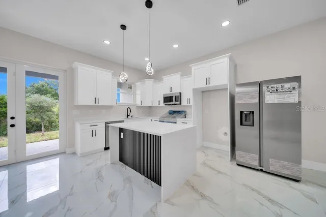 a large kitchen with stainless steel appliances kitchen island granite countertop a refrigerator a sink a stove and white cabinets with wooden floor