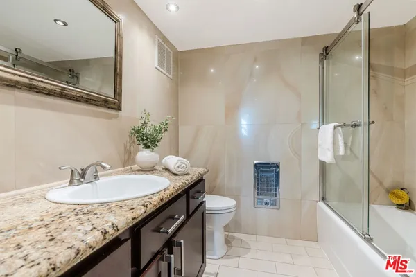 a bathroom with a granite countertop sink a toilet a mirror and shower