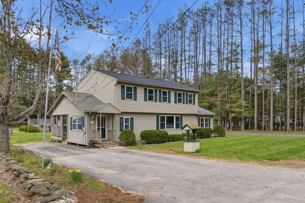 a view of a white house next to a yard with big trees