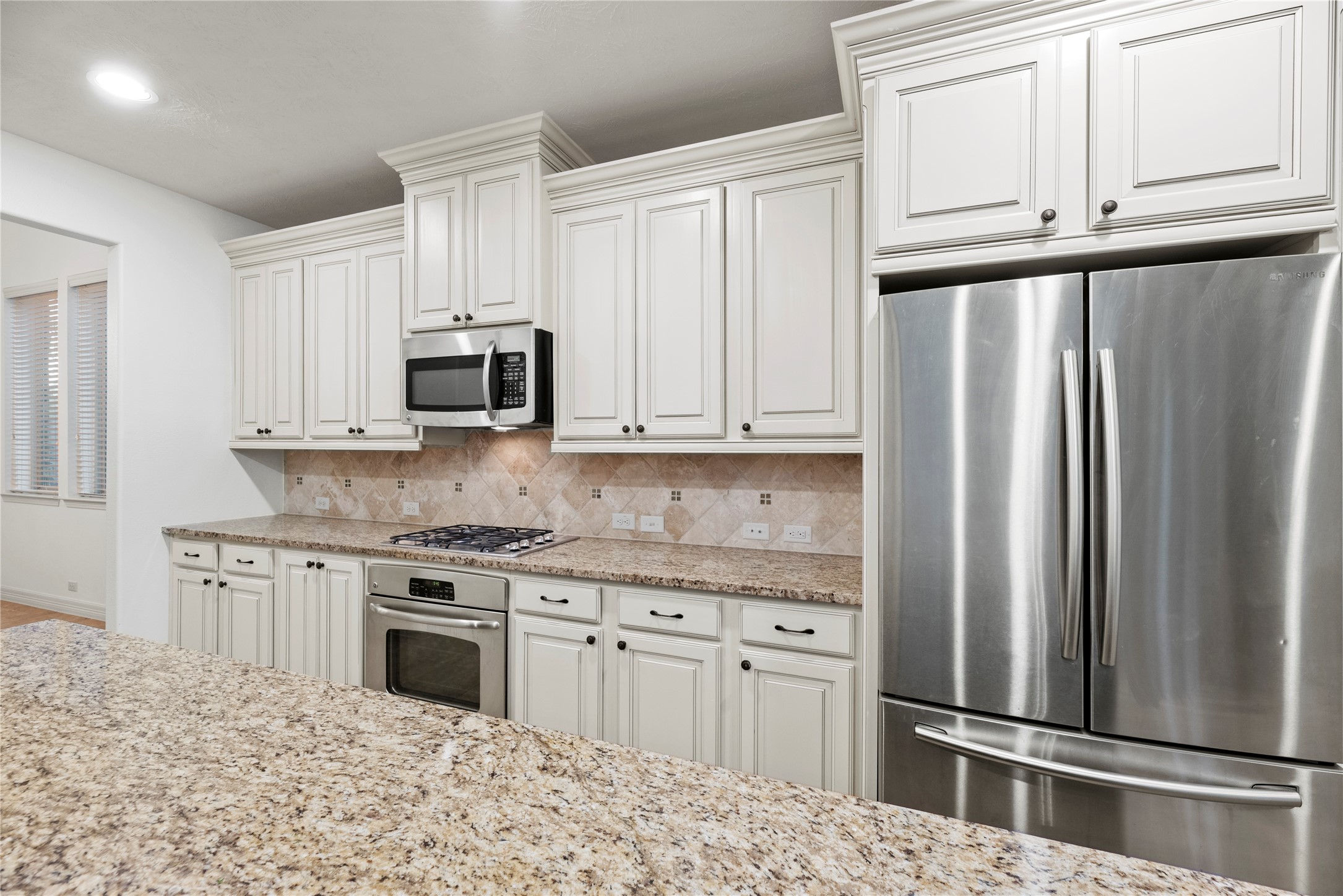 5827 Amherst Farms Lane Fulshear, TX 77441 - Photo 13 of 48 A closer look reveals the beautifully finished cabinetry extending to the ceiling with decorative crown molding. Stainless steel appliances include a French-door refrigerator, built-in microwave, and gas cooktop. The tile backsplash with subtle accent inlays complements the granite countertops and adds warmth and texture to the space.