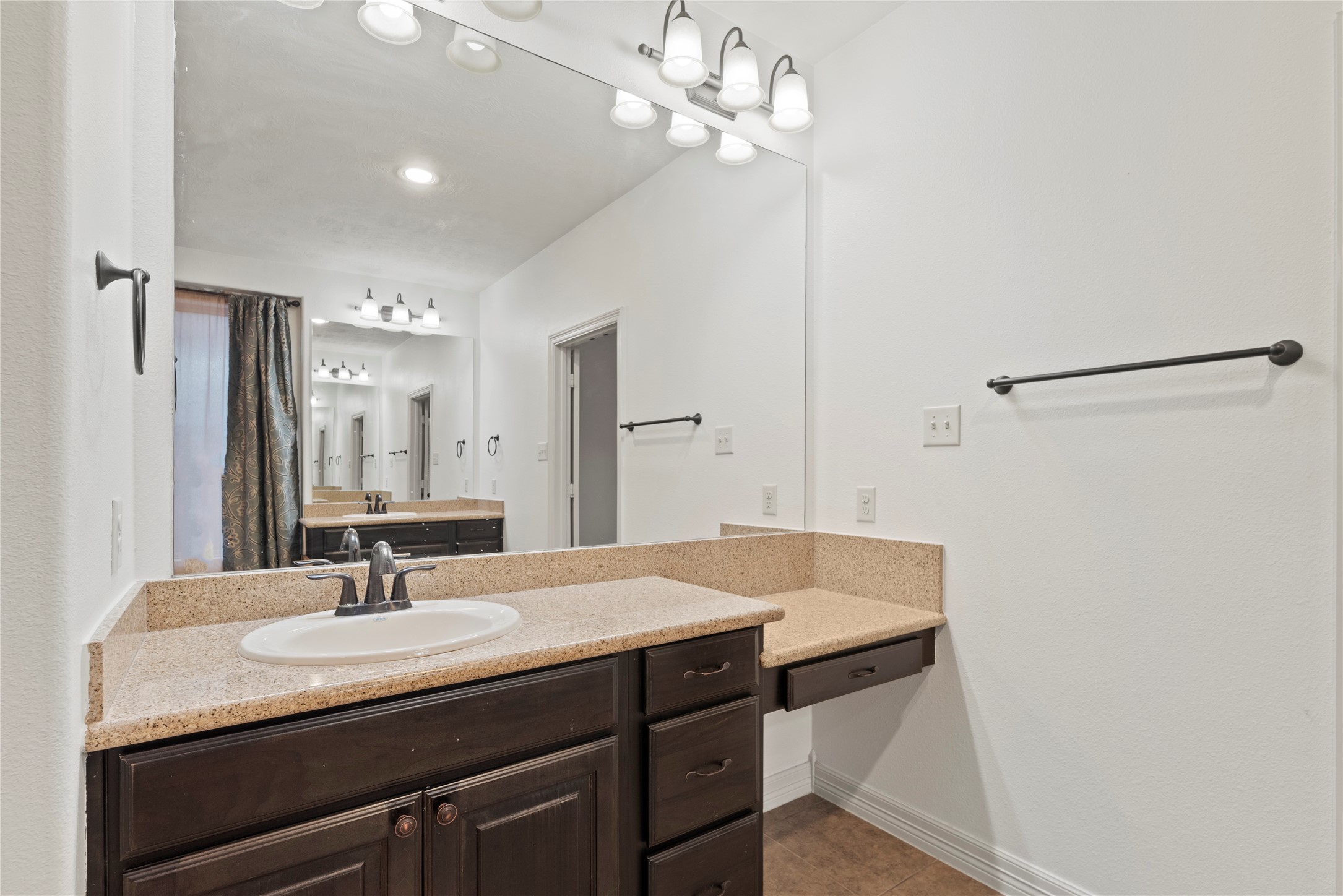 5827 Amherst Farms Lane Fulshear, TX 77441 - Photo 18 of 48 This expansive vanity area showcases abundant counter space with granite surfaces, an undermount sink, and a large wall-to-wall mirror that enhances brightness. A built-in seated makeup vanity provides additional storage and a dedicated space for daily routines.